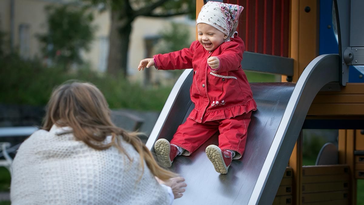 Äiti ottaa liukumäkeä laskevan lapsen vastaan.