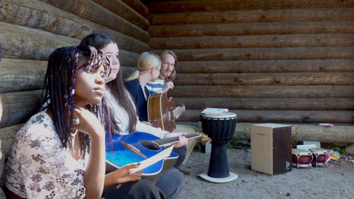 Kolme nuorta soittamassa kitaraa ja rumpuja ulkona