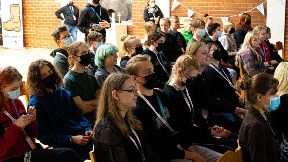 Joukko nuoria istuu katsomossa kuuntelemassa tilaisuutta