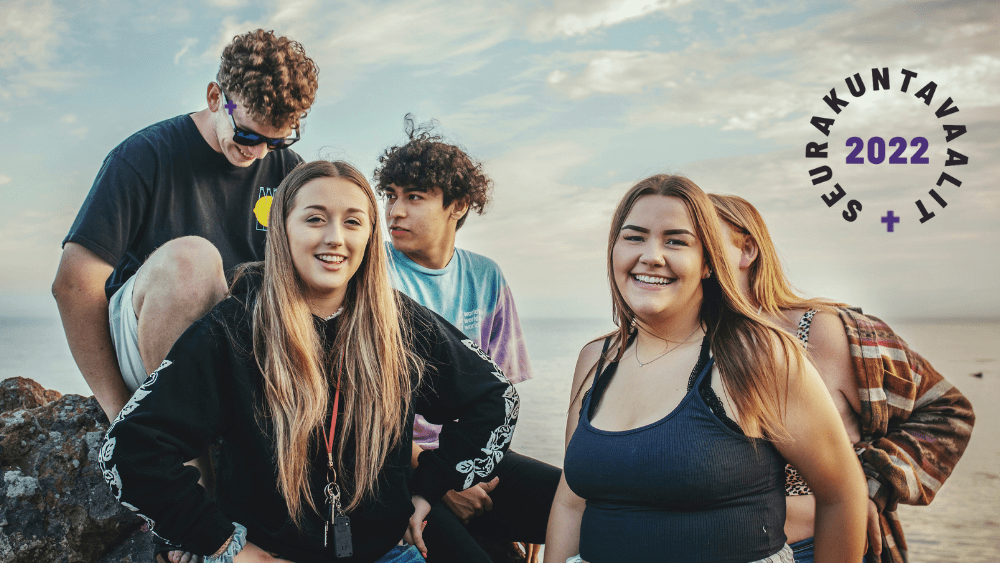 Viisi nuorta ovat kalliolla taustanaan harmaansininen taivas. Eturivissä on kaksi nuorta naisoletettua, joilla on molemmilla pitkät hiukset. Molemmat hymyilevät. Toisella on päällään sininen toppi, toisella musta college-paita. Molemmat ovat valkoihoisia. Heidän takanaan kalliolla istuu kaksi nuorta miesoletettua. Heistä vasemmanpuoleisella on aurinkolasit silmillään ja hän katsoo alaspäin. Hänellä on kiharat hiukset, valkoinen iho ja musta t-paita. Hänen oikealla puolellaan olevalla henkilöllä on tummanruskeat kiharat hiukset, ruskea iho ja sinivioletti pastellinsävyinen T-paita. Hänen oikealla puolellaan on henkilö, jonka eturivissä oleva pitkähiuksinen nainen peittää lähes kokonaan. Näkyy vain punavalkoruutuinen flanellipaita ja pitkät, vaaleat hiukset.