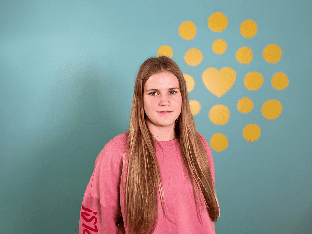 Läheltä otettu kuva nuoresta. Nuori seisoo koristeseinän edessä ja katsoo kameraan.