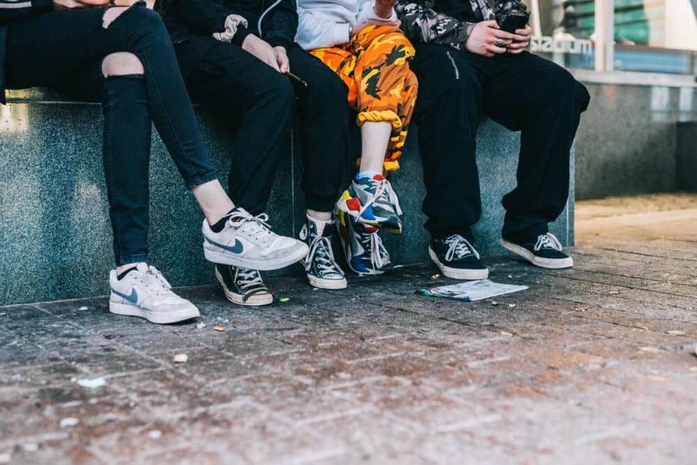 Kuvassa näkyy nuorten jalkoja. He istuvat vierekkäin rivissä.