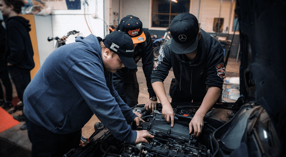 Kolme nuorta korjaavat auton moottoria.