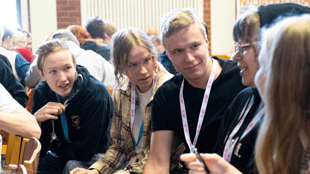 Nuoret istuvat vierekkäin. Yksi nuorista puhuu ja muut kuuntelevat kiinnostuneina.