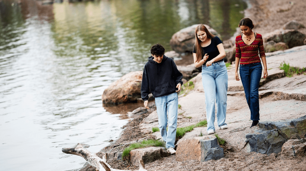 Kolme nuorta kävelevät vesistön rantaa pitkin ja keskustelevat.