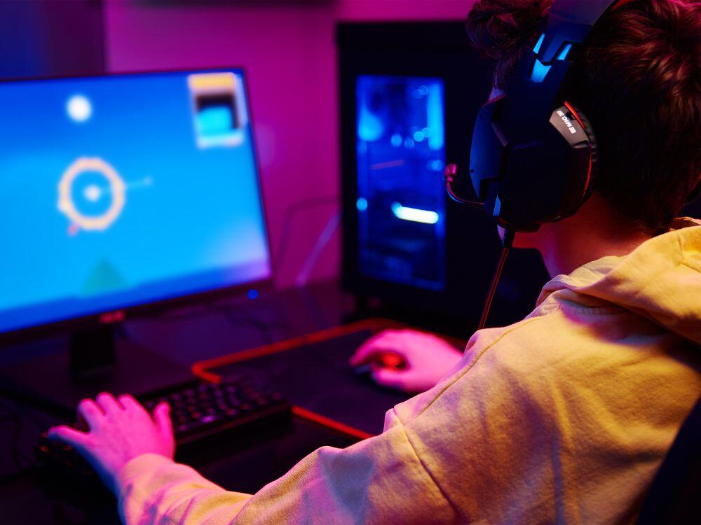 Nuori pelaa tietokoneella kuulokkeet korvilla.