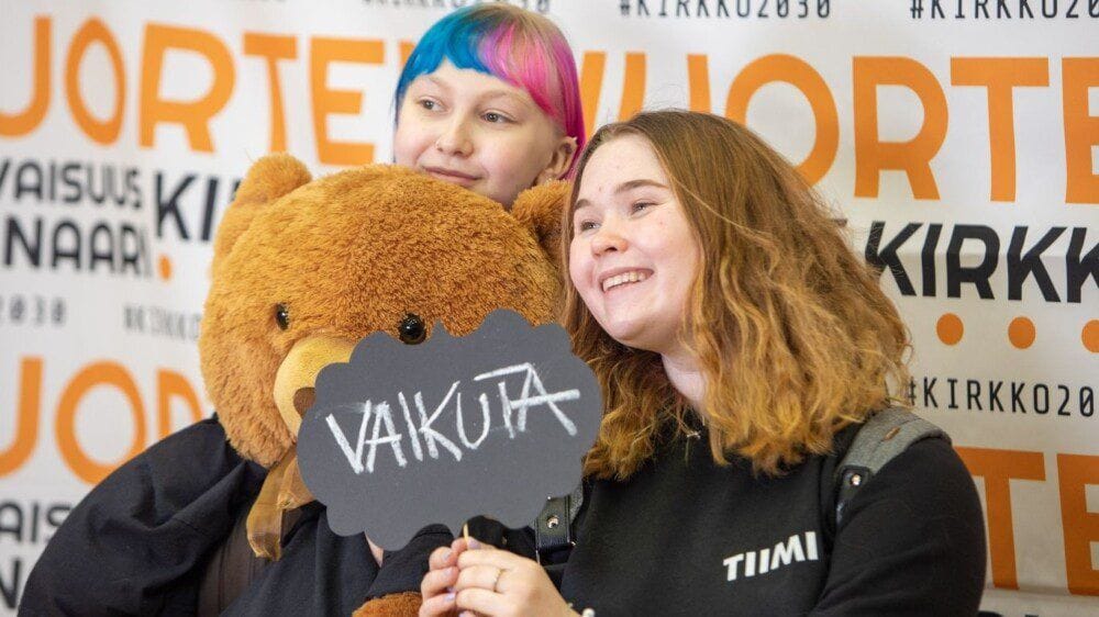 Kaksi nuorta poseeraavat Tulevaisuusseminaarin valokuvausseinän edessä nallen ja kyltin kanssa, jossa lukee "vaikuta".