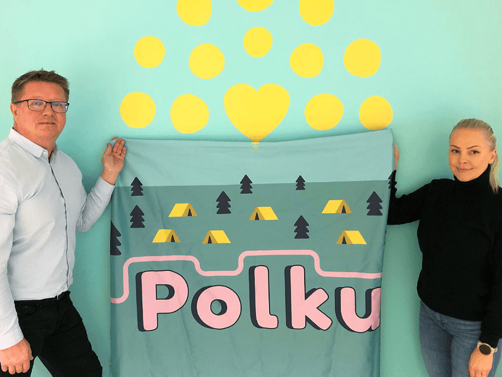 Kuvassa Polkuleirin vastaavat työntekijät. Vasemmalla Veijo Kiviluoma ja oikealla Satu Rathgeber, jotka pitelevät Polkuleirin banneria käsissään.