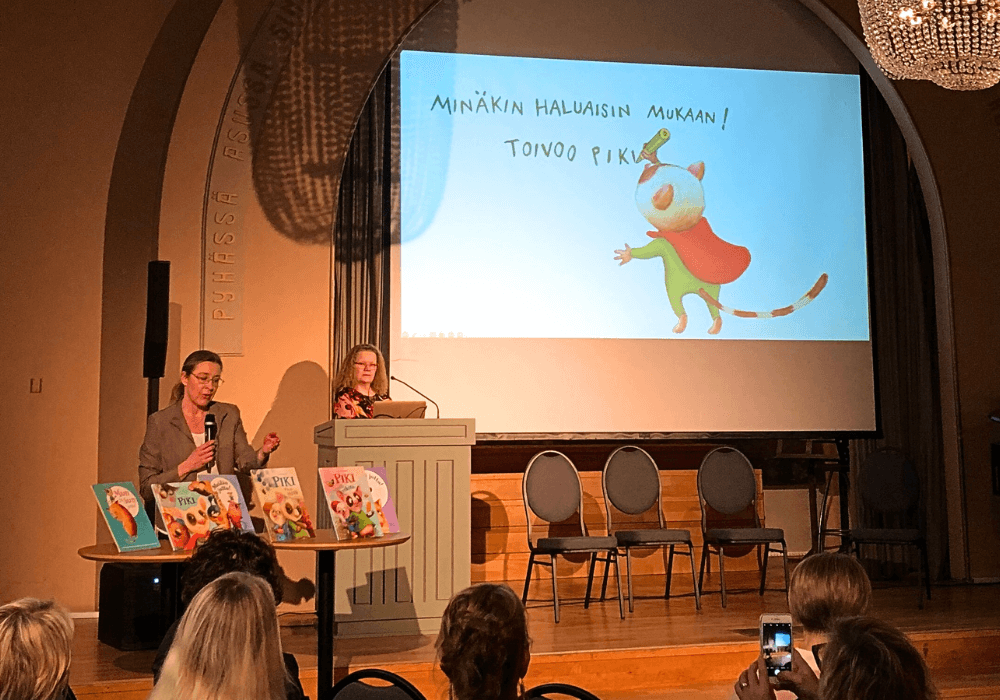 Lasten kiusaamisen ehkäisy -seminaari. Katariina Elomaa ja Tiina Haapsalo pitävät esitelmää Piki-toimintamallista. Seinälle on heijastettu esityksen diat, joissa näkyy Piki-hahmo.