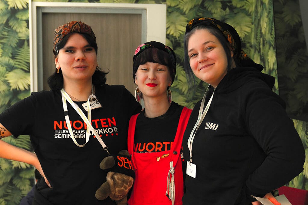 Kolme nuorta katsovat hymyillen kameraan. Nuorten paidoissa näkyy Nuorten tulevaisuusseminaarin logo.