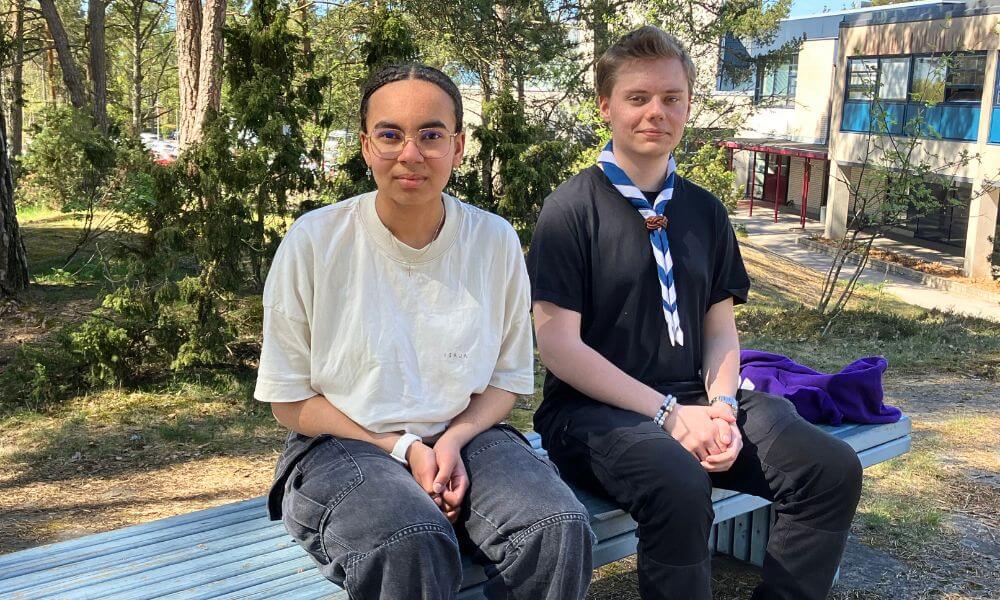 Kaksi nuorta istuvat penkillä ulkona.