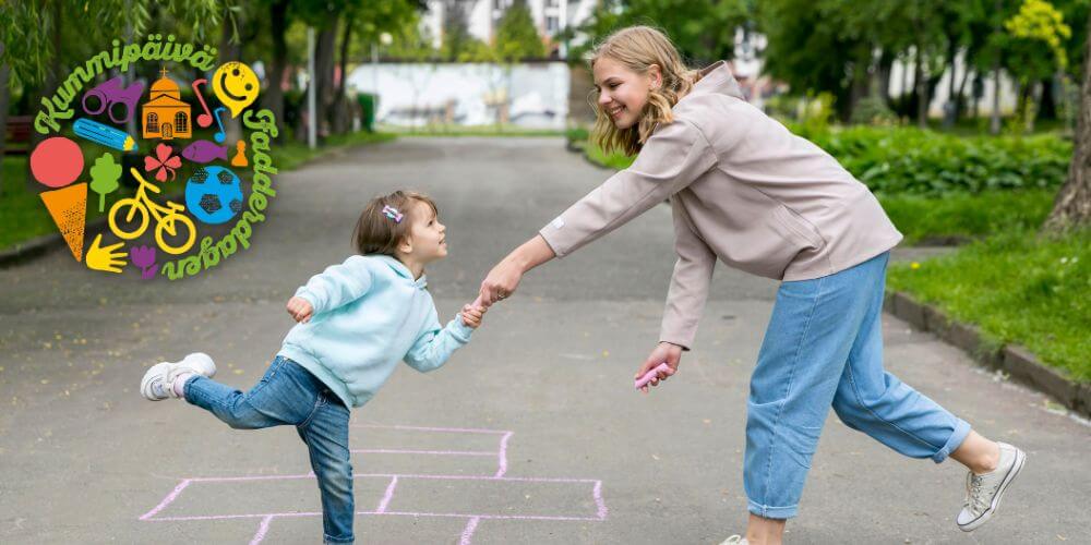 Lapsi ja aikuinen hassuttelevat ulkona. Taustalla Kummipäivän logo.