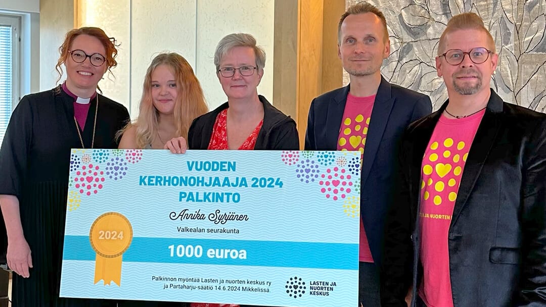 Vuoden kerhonohjaaja kädessään suuri palkintoshekki. Rinnalla palkinnon luovuttajat