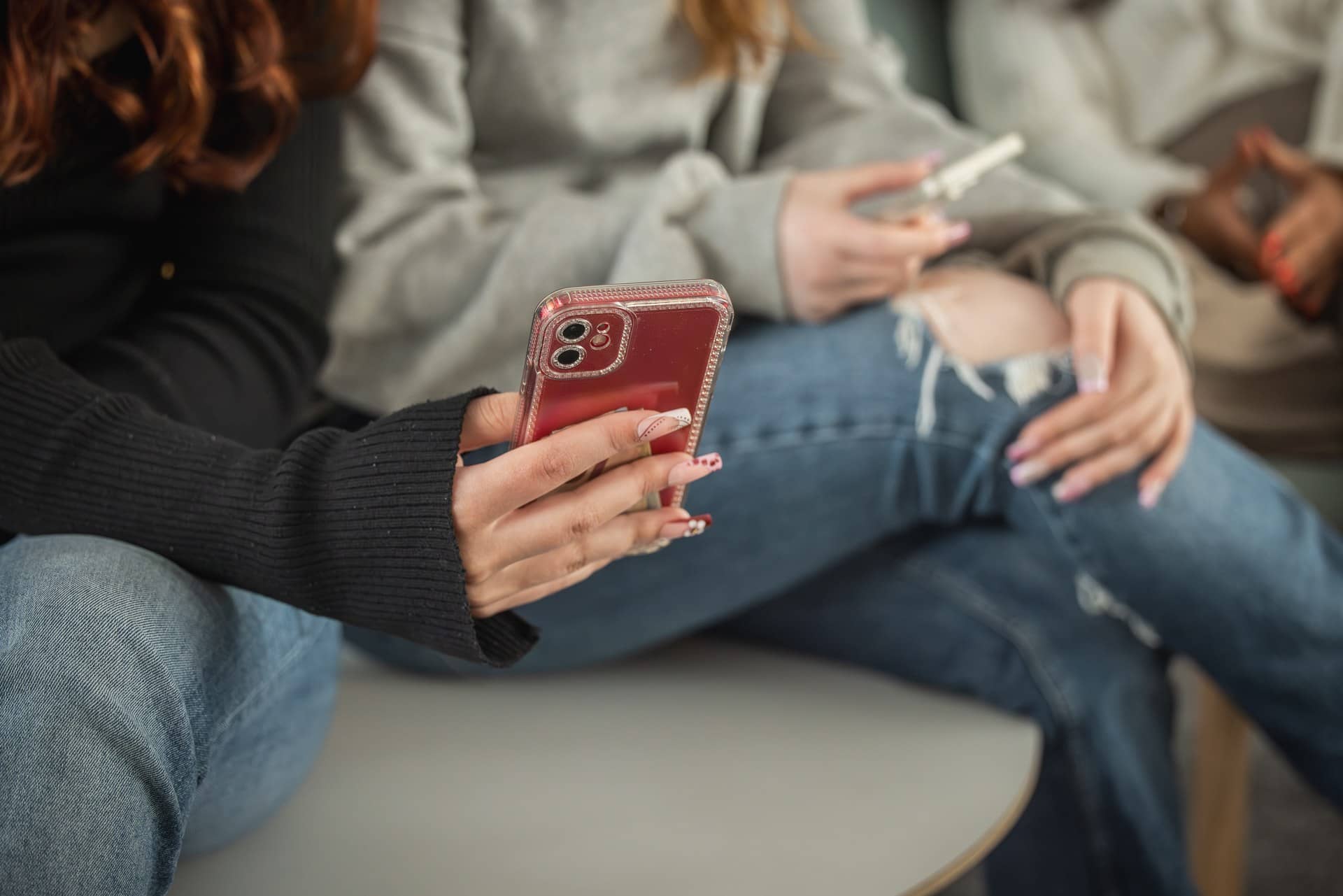 Nuoria naisoletettuja henkilöitä istumassa ja katsomassa puhelimia.