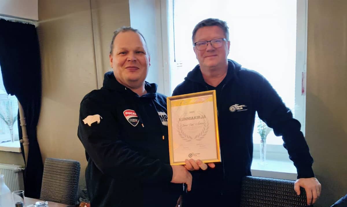 Kaksi henkilöä pitämässä Moottoripajan kunniakirjaa esillä.