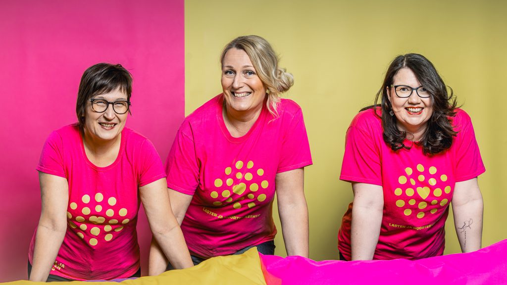 Kolme Pikkuhelppi-työntekijää pinkeissä paidoissa.