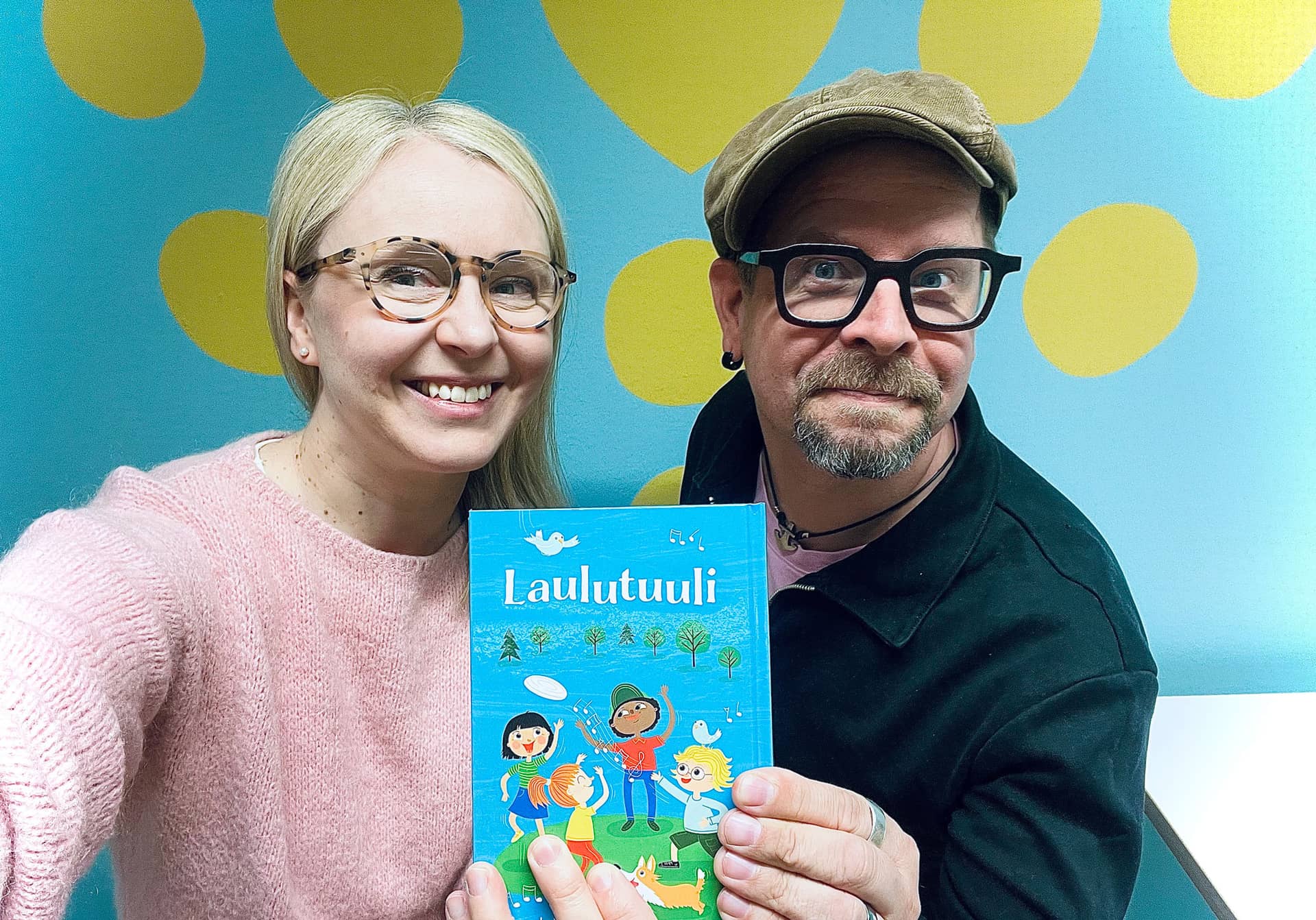 Kaksi henkilöä pitävät kiinni kirjasta, jossa lukee Laulutuuli.